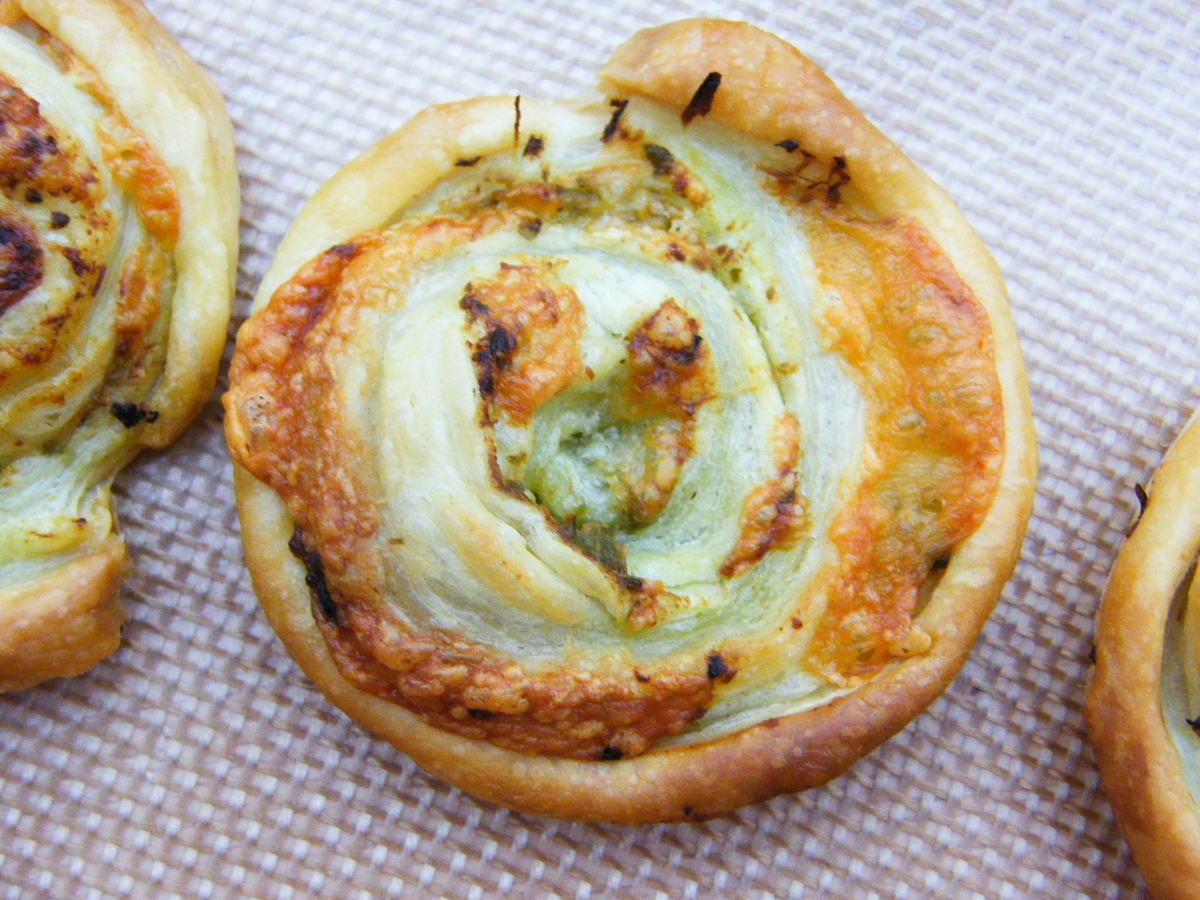 Close up of pastry cheese and pesto swirl on a baking sheet.