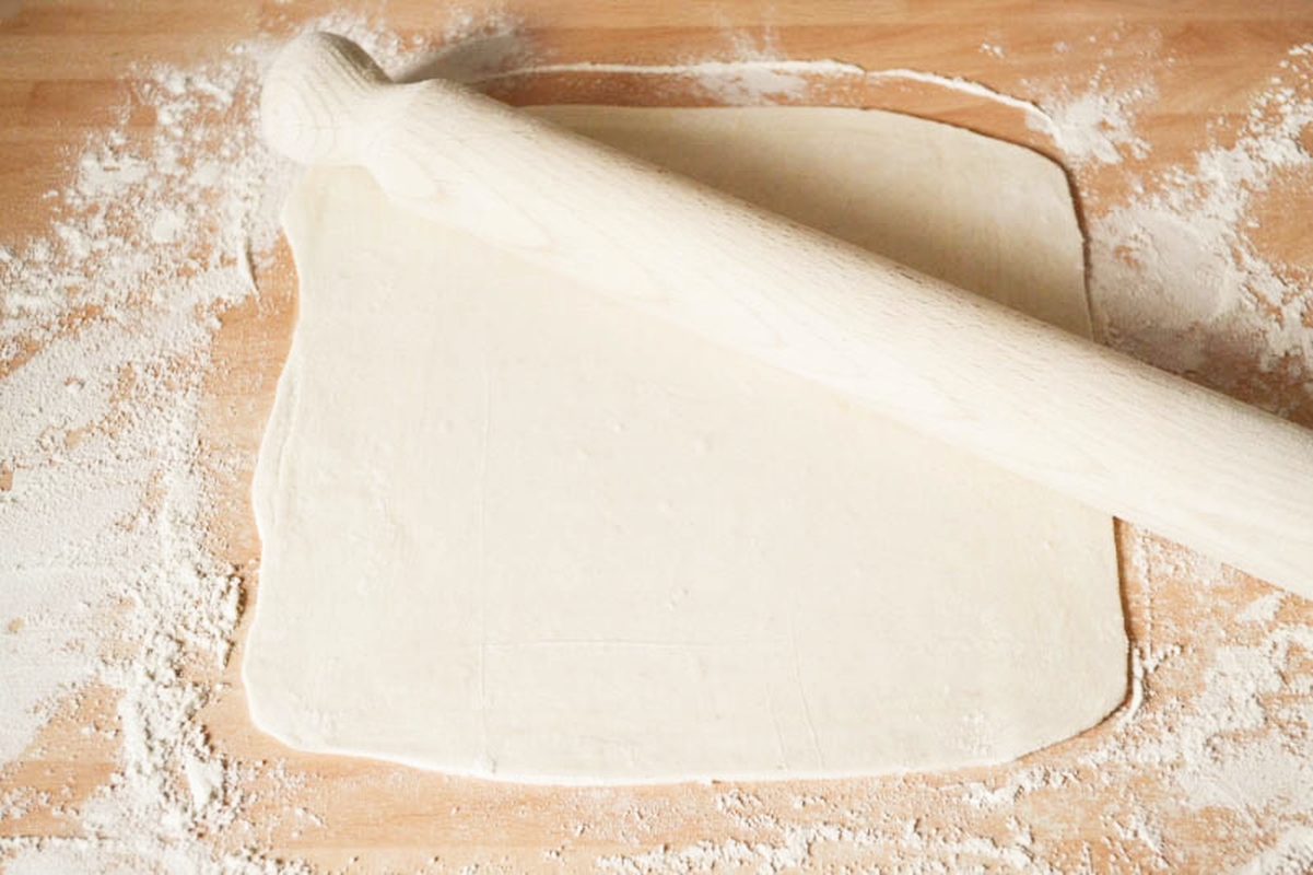 pastry rolled out with a rolling pin on a floury surface.