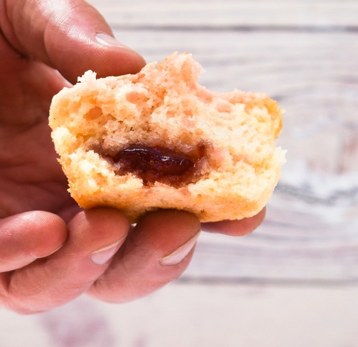 man holding half a strawberry muffin showing jam filling.
