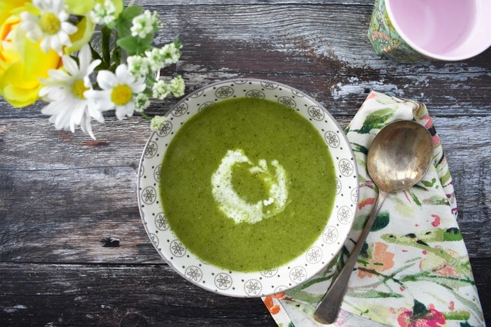 Vibrant green broccoli and pea soup served with a swirl of cream.
