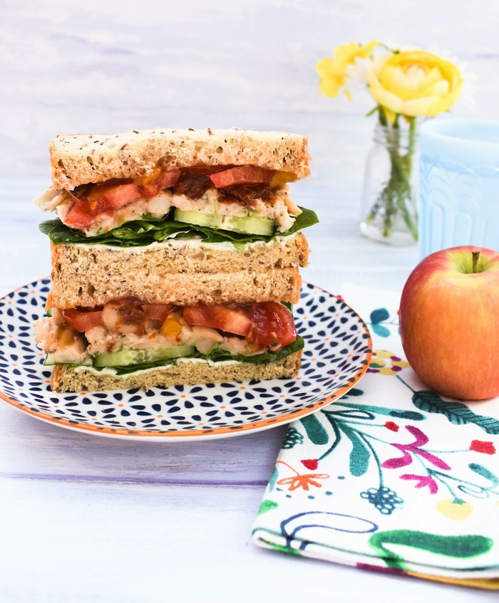 white bean & tomato sandwich served with a red apple.