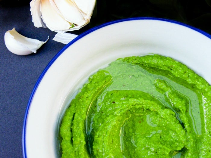 Vibrant green vegan Cashew Pesto in a bowl next to a head of garlic.
