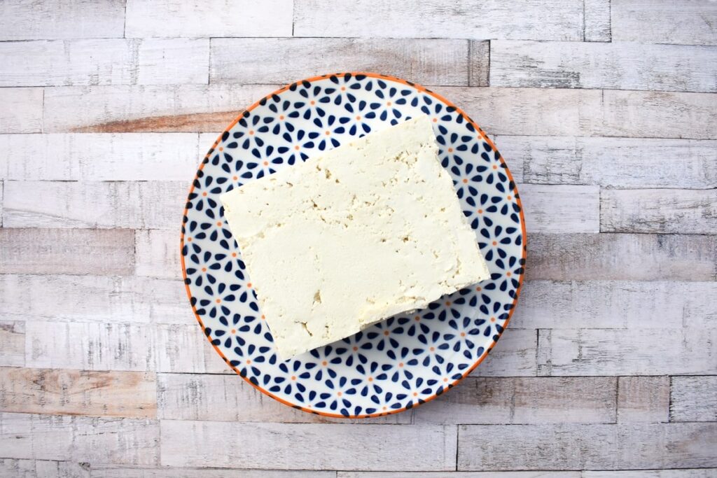 A block of firm tofu on a pattered plate