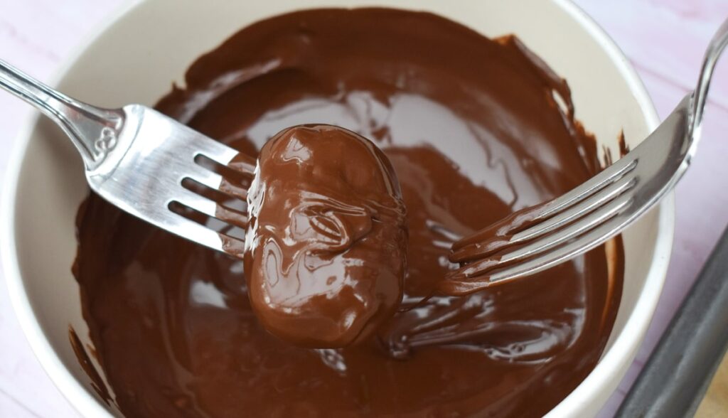 snickers bites lowered into melted chocolate on forks