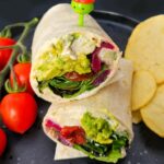 Easy Avocado & Hummus Lunch Wraps on a plate with cherry tomatoes and crisps.