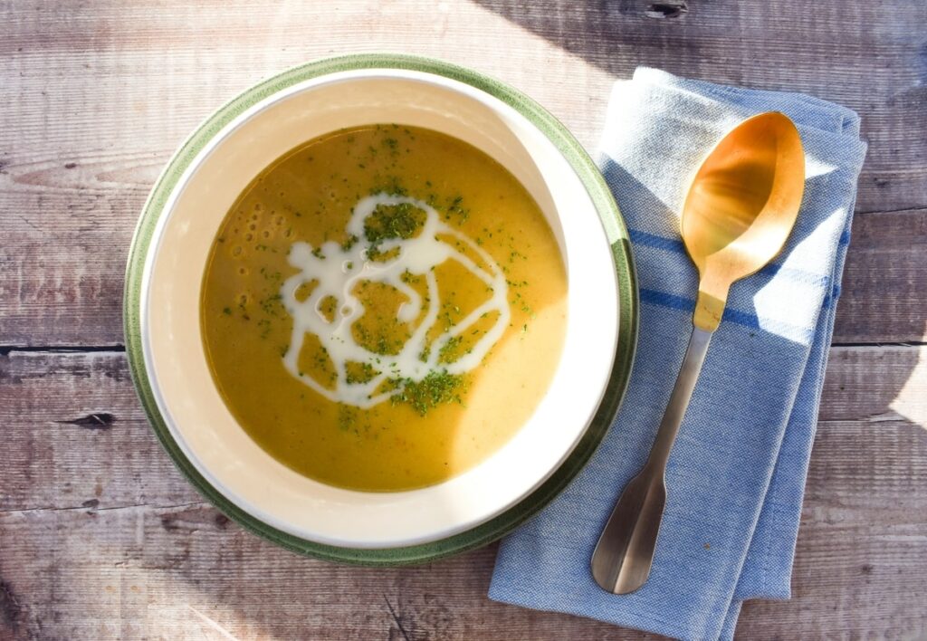 Baked Tattie Soup. in a bowl topped with a drizzle of oat milk and herbs.