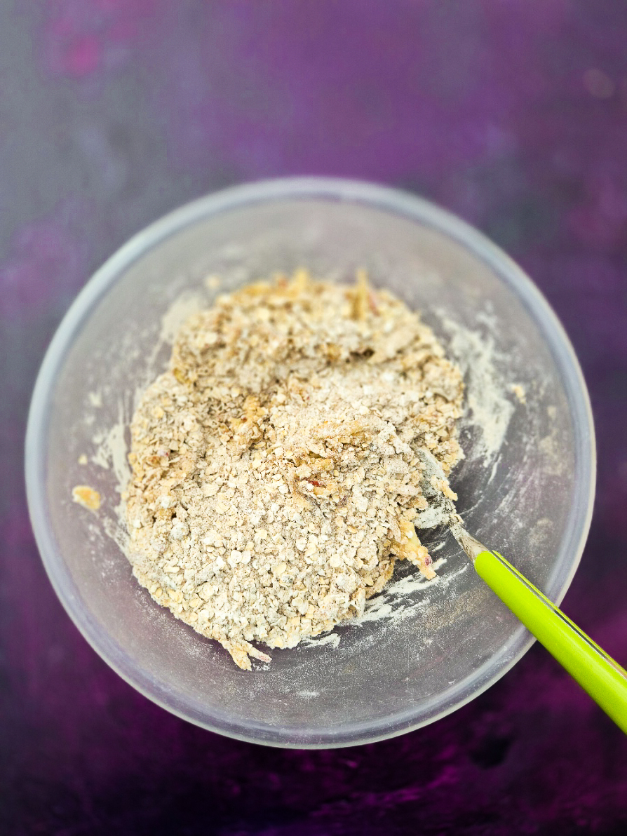 Fresh apple mixed into dry flapjack mixture in mixing bowl.